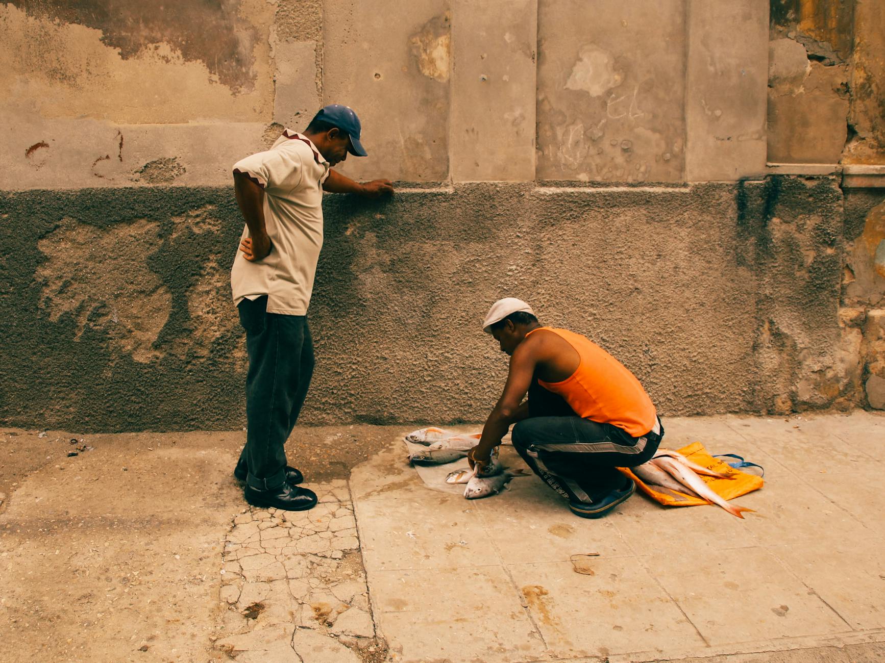 A street vendor gutting fish on an urban pavement with an onlooker, showcasing small business dynamics.