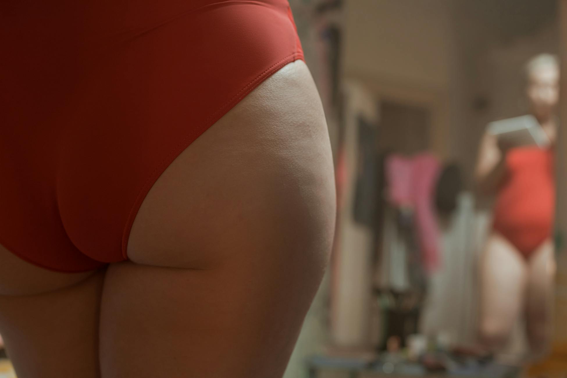A close-up view of a person embracing body positivity in red swimwear, self-reflecting in a mirror.